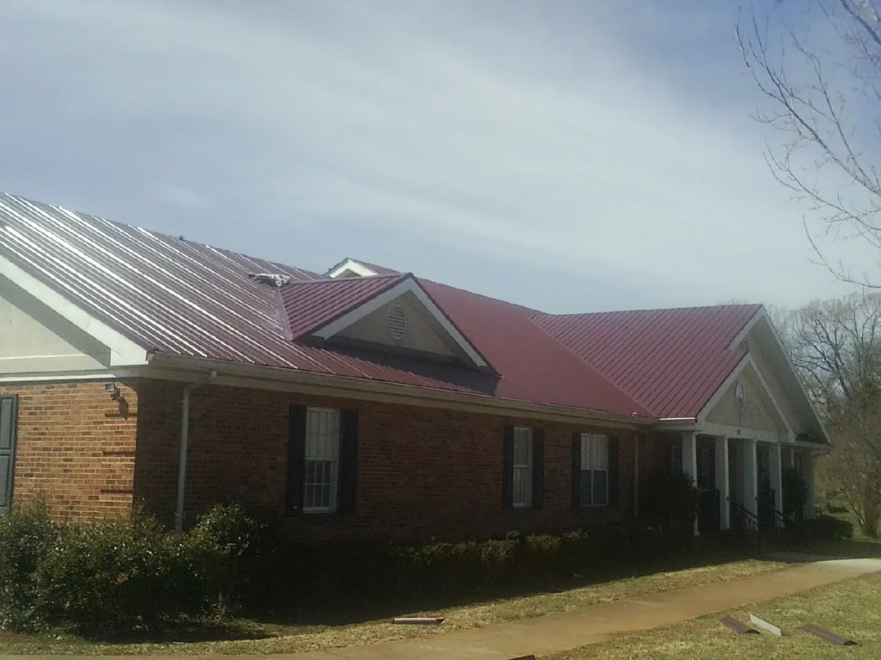 Red metal roof with gabled entries on a long brick building, from a Hail Damage Roof Repair job in Leon